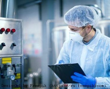 Technologist expert in protective uniform with hairnet and mask taking parameters from industrial machine in food production plant.